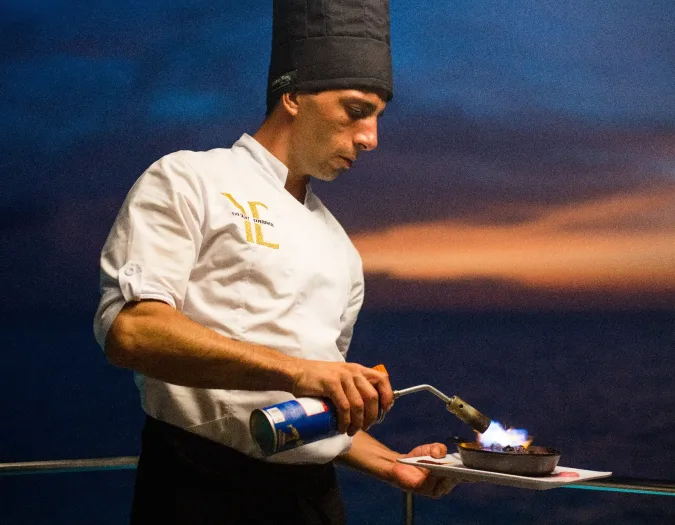 Onboard chef torching a dish at sunset